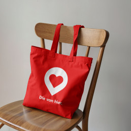 Stofftasche mit dem Locator und dem Kampagnenslogan Die von hier im Sparkassen look auf braunem Holzstuhl