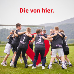 Kinderfu&szlig;ballteam springen lachend um den Pin der Sparkasse Werra-Mei&szlig;ner, Motiv f&uuml;r die Kampagne der Sparkasse Die von hier, gesponsert von der lokalen Sparkasse