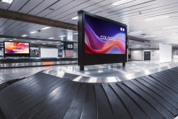 Gepäckausgabe am Flughafen, Bildschirme zeigen die Videos der Ticketkampagne der DMEXCO 2026