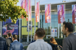 Eingang Nord der Kölnmesse, Fahnen mit DMEXCO Logo und Farbverlauf, Menschen im Vordergrund laufen zu den Eingängen
