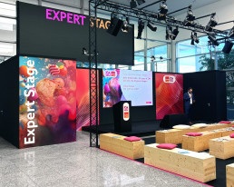 B&uuml;hne auf der ISM, Expert Stage mit Visual als Hintergrund und Logo-Kombination, Holzkuben als Sitzgelegenheit