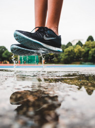 Beine und Schuhe einer Sportlerin, die in eine Pf&uuml;tze springt, spritzendes Wasser, Spiegelung in der Pf&uuml;tze