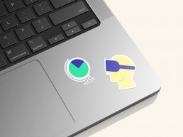 Illustrative Sticker der Marke qoodos in gelb, gr&uuml;n und blau. Auf einem Macbook aufgeklebt