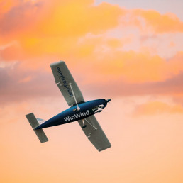 Fliegendes Propellerflugzeug in orange gelben Wolken, Schriftzug auf der unteren Seite des Flugzeuges auf Fl&uuml;gel und Rumpf