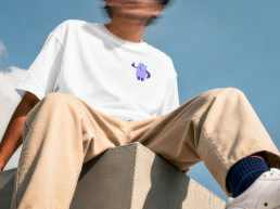 Junger Mann sitzt auf Steinkante, Kopf in Bewegungsunsch&auml;rfe, kleine lilafarbene Monsterillustration auf wei&szlig;em Tshirt