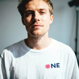 Junger Mann schaut in die Kamera, seitliches Licht, Wei&szlig;es Shirt mit Schriftzug one