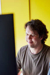 Mitarbeiter der Content Refinery, Mann am Computerbildschirm, gelbe R&uuml;ckwand